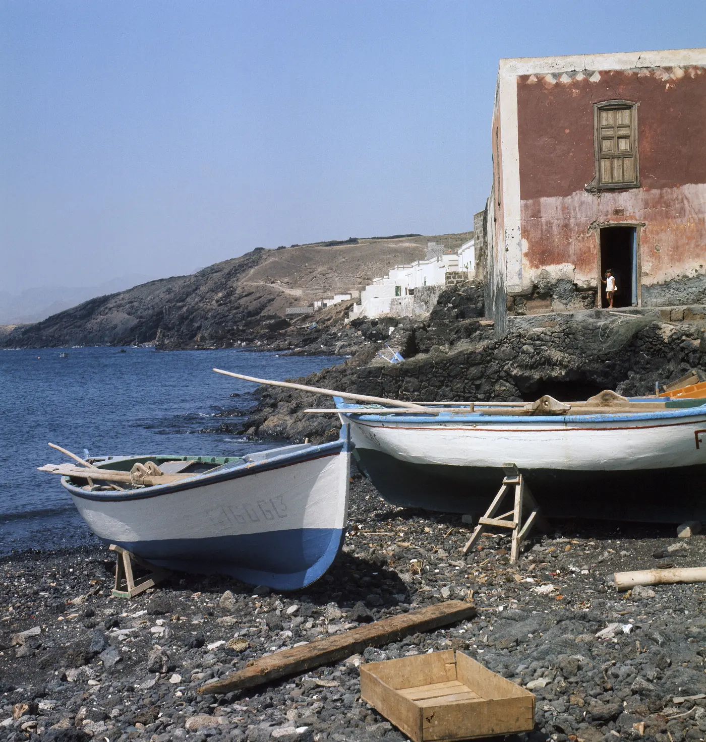 White houses below a red cliff with boats on the shore