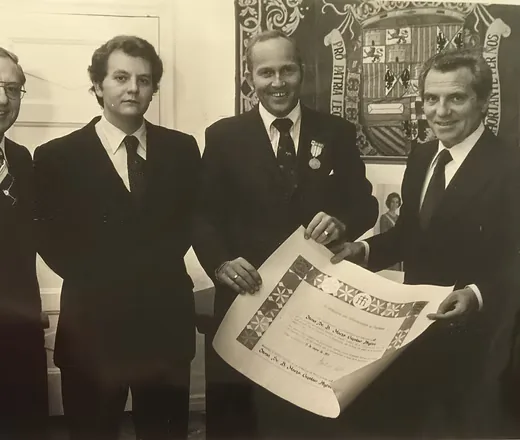 A diploma being presented in front of the Spanish coat of arms